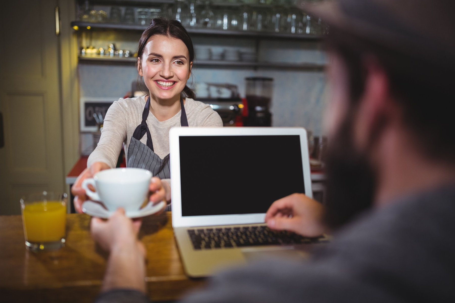 Kawiarnia – baristka podaje kawę klientowi z laptopem